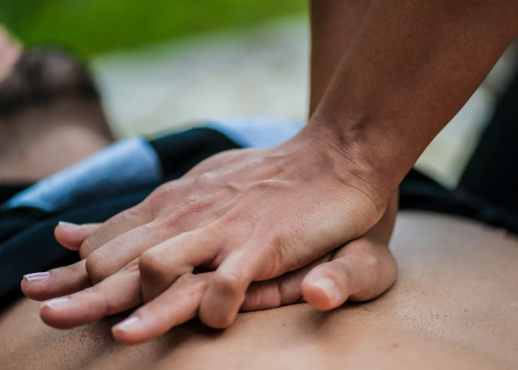 A man lies flat while someone does CPR on his bare chest jpg