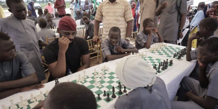 Onakoya and the children playing chess at Malhohi IDP camp in Adamawa State.