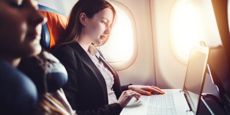 Female entrepreneur working on laptop sitting near window in an airplane.