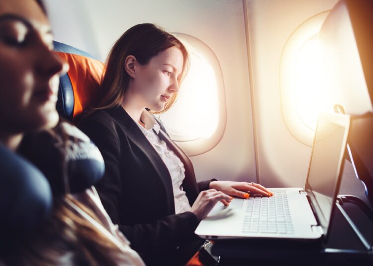 Female entrepreneur working on laptop sitting near window in an airplane.