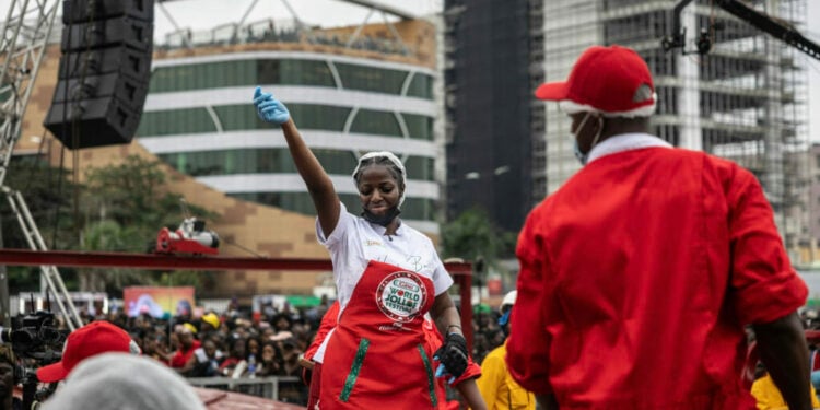 Nigerian chef Hilda Baci (L) dances as she stands next to a giant pot during an attempt to break the world record for the largest pot of Jollof rice, led by Nigerian chef Hilda Baci in Lagos, on September 12, 2025. (Photo by OLYMPIA DE MAISMONT / AFP)