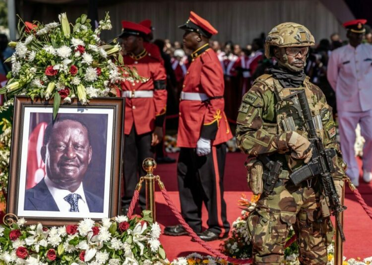 A soldier from the Kenya Defence Forces (KDF) stands beside a portrait of Kenyas opposition leader Raila Odinga as military personnel guard his coffin during the final day of his funeral proceedings at Jaramogi Oginga Odinga University grounds in Bondo, on October 19, 2025. Odinga, 80, died from a suspected heart attack in India on October 15, 2025, triggering a huge outpouring of grief across the country, but particularly in western Kenya where his Luo tribe is dominant. (Photo by Luis TATO / AFP)