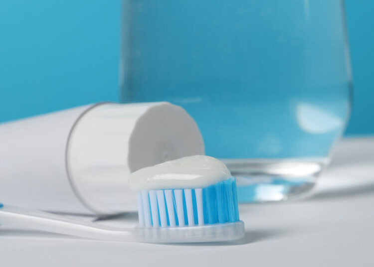 Firm Advocates Fluoride Use For Better Oral Health 1 Plastic toothbrush with paste and glass of water on white table against light blue background, closeup
