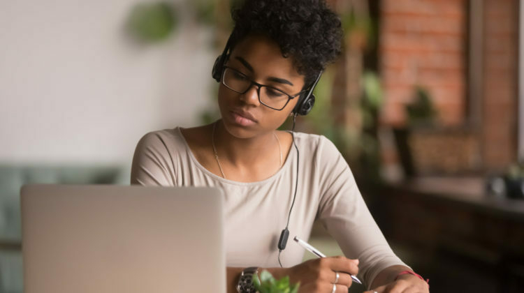Tech Leaders Demand Safer Digital Spaces For Women 1 Focused mixed race woman wearing headphones watching webinar write notes study online with skype teacher, african female student learning language computer course on laptop listen translate lecture