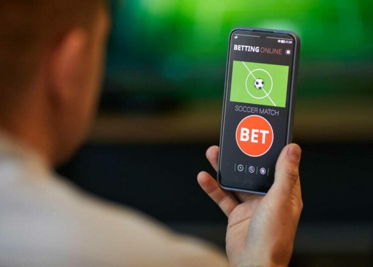 Are Mobile Bettors Predicting Reality… or Predicting Other Bettors? 1 Person holding phone with soccer betting app open.