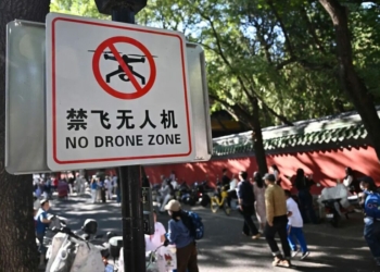 People walk past a sign reading “No drone zone” in an alley in Beijing on September 14, 2026. Beijing will ban the possession of drones within city limits under new rules from November, further tightening regulations that already prohibited the sale of the devices. (Photo by Pedro PARDO / AFP)