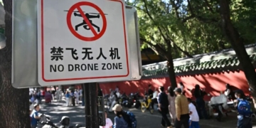People walk past a sign reading “No drone zone” in an alley in Beijing on September 14, 2026. Beijing will ban the possession of drones within city limits under new rules from November, further tightening regulations that already prohibited the sale of the devices. (Photo by Pedro PARDO / AFP)