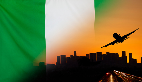 Travel and transport concept with skyline silhouette, highway traffic and airplane at sunset merged with real fabric flag of Nigeria